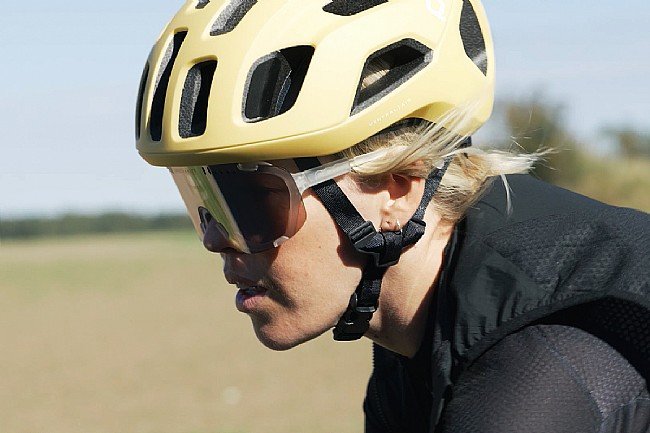 Side profile of a cyclist wearing stylish yellow cycling glasses and helmet, mid-ride against a soft-focus natural backdrop @ Bici.