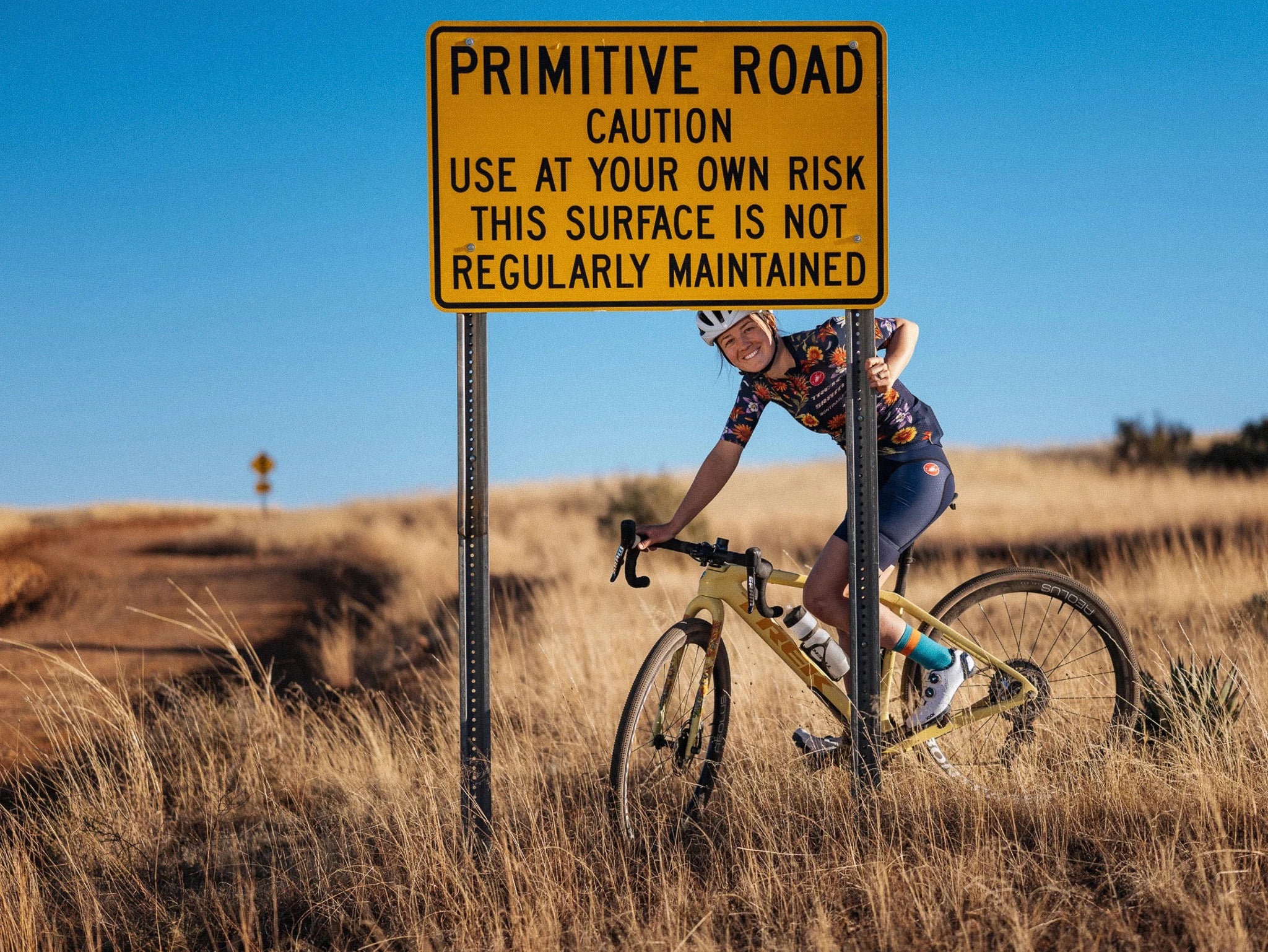 Cyclist riding a Trek bike on a rustic trail by a 'Primitive Road' sign, showcasing the adventurous spirit of Trek bikes @ Bici.