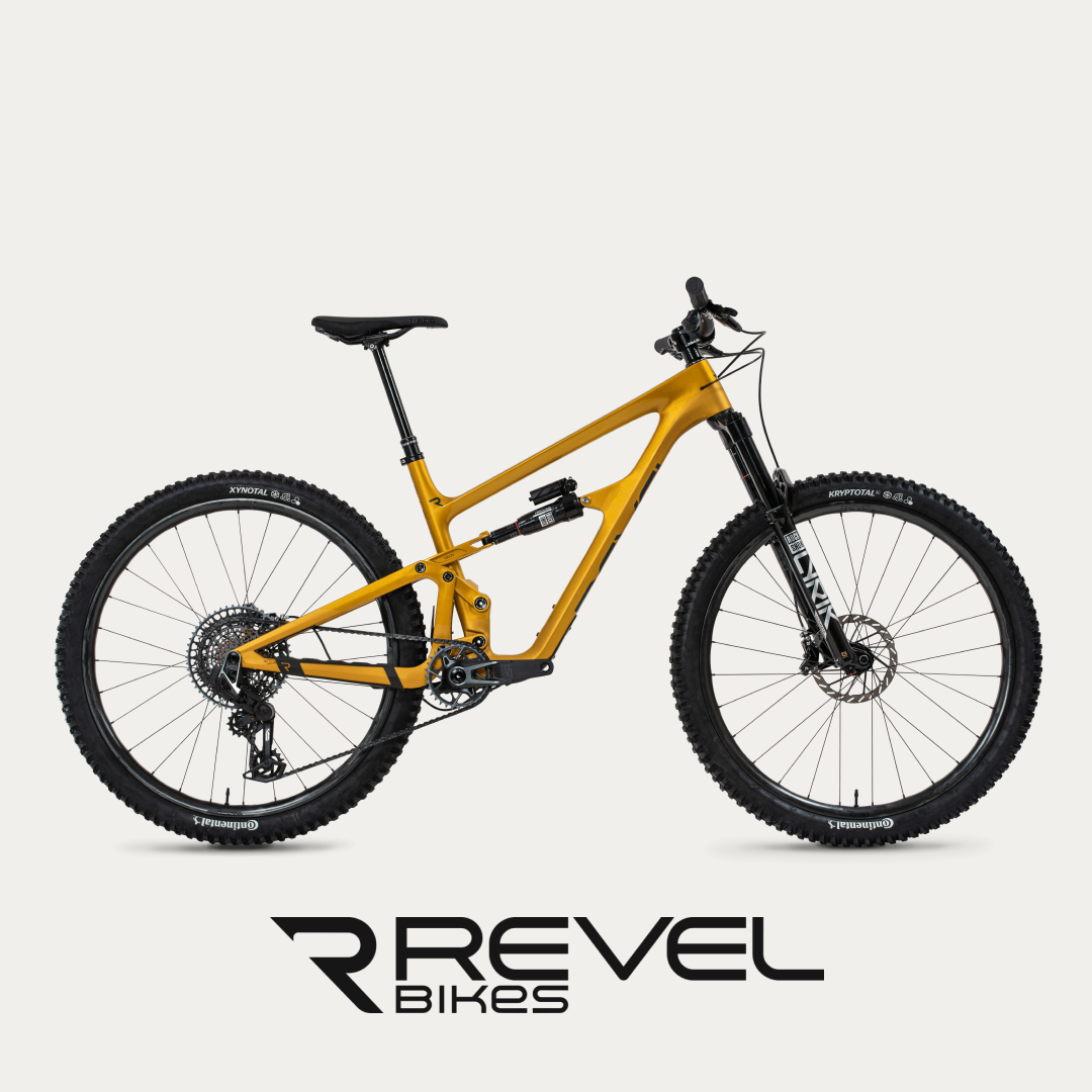 The bold Revel mountain bike stands out with its vivid golden frame, full-suspension setup, and robust tires for all-terrain riding @ Bici.
