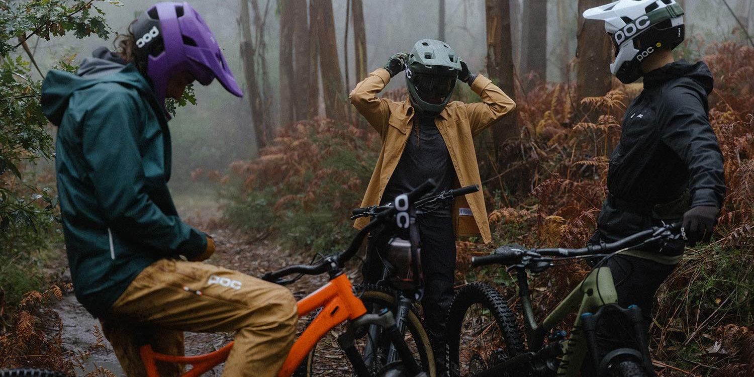 Mountain bikers in a misty forest, one adjusting a full-face helmet, the other ready to ride @ Bici.