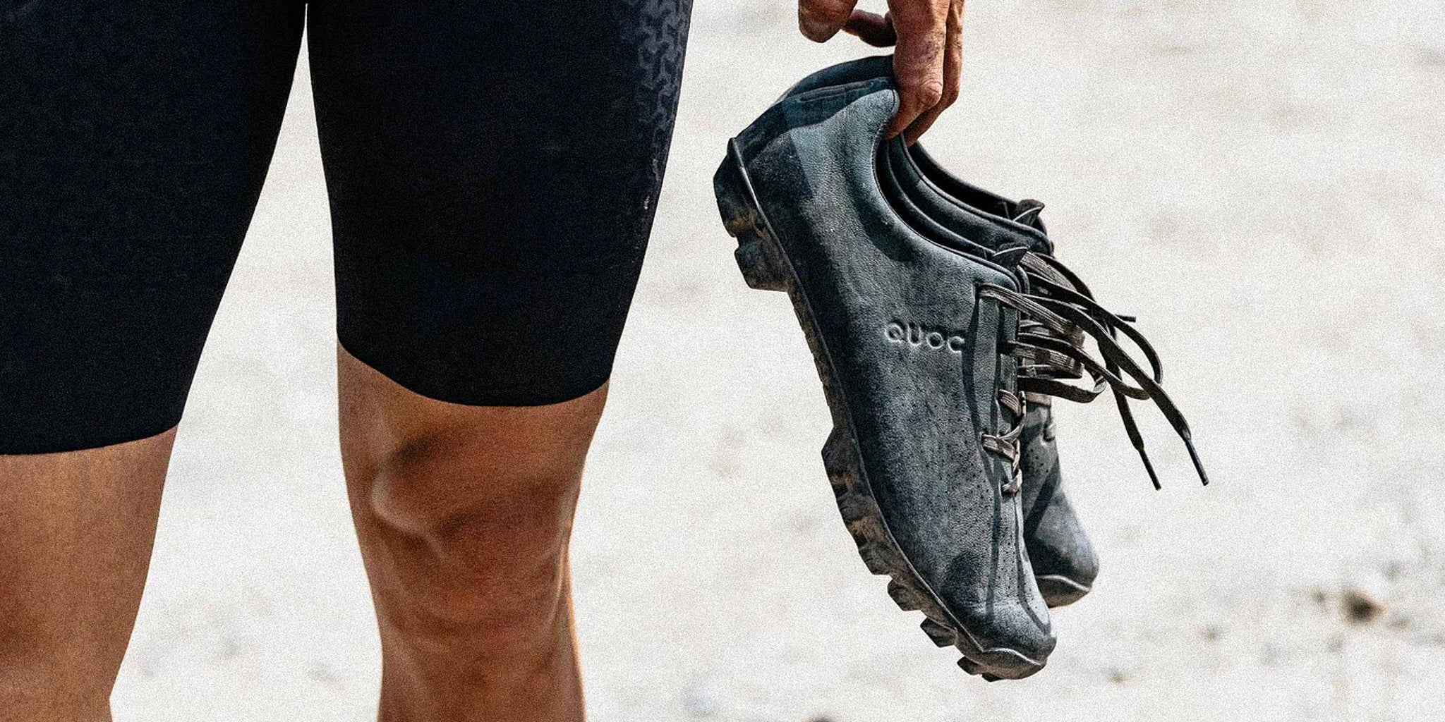 Cyclist holding a pair of worn-in QUOC mountain biking shoes, highlighting the rugged sole and secure lacing @ Bici.