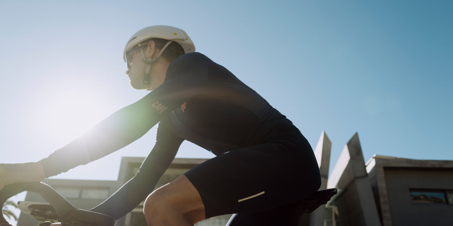 Focused cyclist wearing aerodynamic helmet and black cycling jersey riding a road bike, blurred urban background @ Bici.