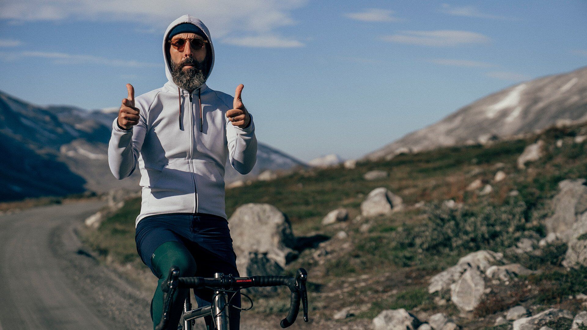 Man giving two thumbs up in a scenic mountainous landscape, symbolizing Bici's commitment to exhilarating cycling experiences and community connection @ Bici.