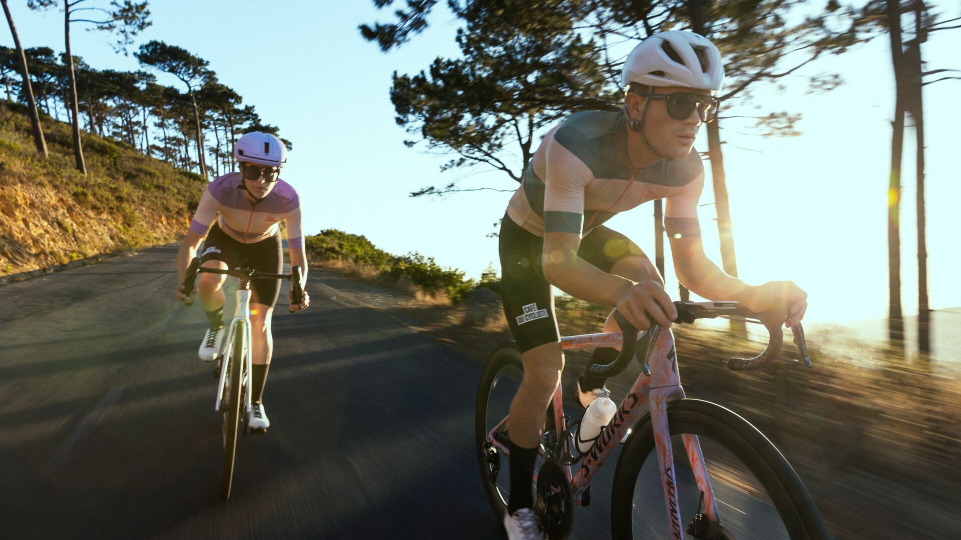 Two cyclists in sync, leading the way on a sunlit road ride, with the focus on the lead rider's determination @ Bici.