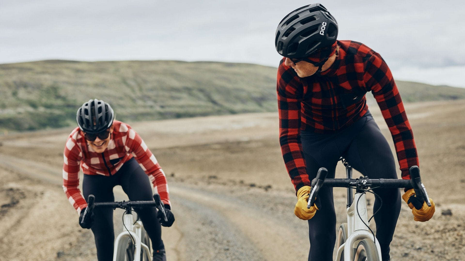 Gravel cyclist in a red flannel jersey, riding with focus and determination on a rugged trail @ Bici.